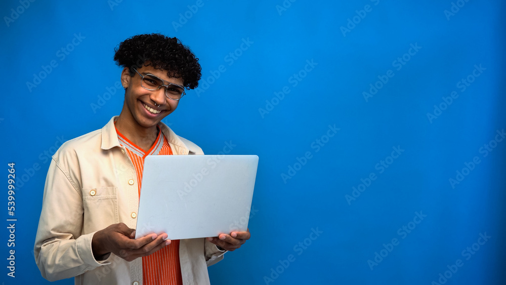 Cheerful and stylish african american freelancer holding laptop isolated on blue Cheerful and stylish african american freelancer holding laptop isolated on blue