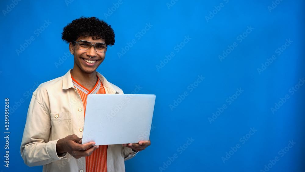 Smiling african american freelancer looking at camera and holding laptop on blue background Smiling african american freelancer looking at camera and holding laptop on blue background