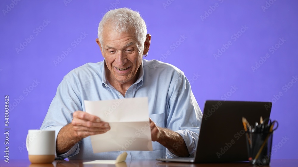 Portrait of happy excited male elderly man opening mail letter reading good news celebrating success, receiving loan approval, salary bonus, get promoted concept isolated on solid purple background Portrait of happy excited male elderly man opening mail letter reading good news celebrating success, receiving loan approval, salary bonus, get promoted concept isolated on solid purple background