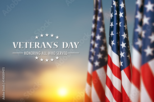 American flags with Text Veterans Day Honoring All Who Served on sunset background. American holiday banner.