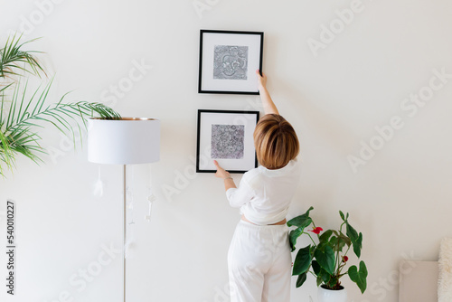 Obraz na plátně Woman hanging pictures on wall in room. Interior design.