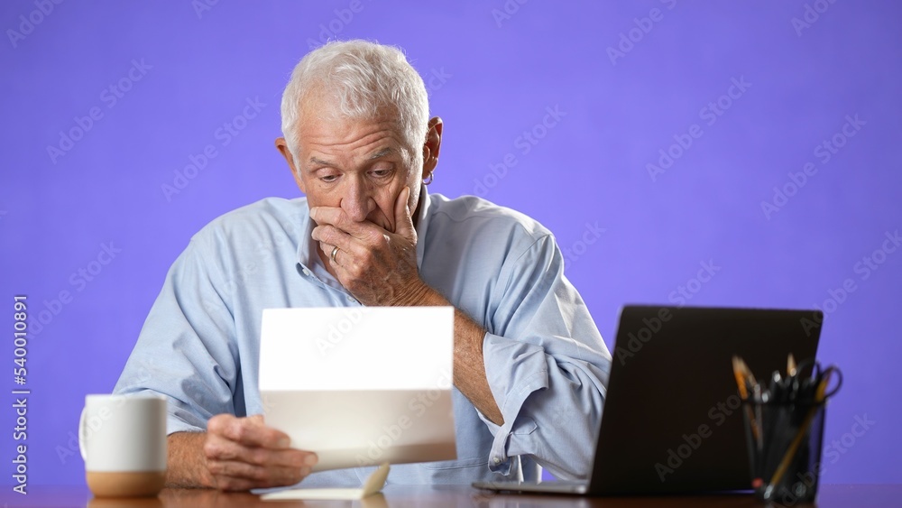 Angry stressed elderly man 70s, opening envelope reading bad news in mail letter. Mad man feels frustrated about high bills, bank debt, tax invoice or mistake isolated on purple background Angry stressed elderly man 70s, opening envelope reading bad news in mail letter. Mad man feels frustrated about high bills, bank debt, tax invoice or mistake isolated on purple background