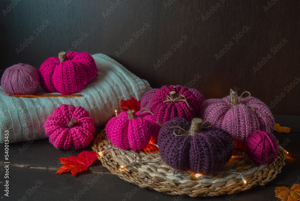 pink colored crochet pumpkins with autumn leaves on dark brown wooden ground with crochet hook and woolen balls