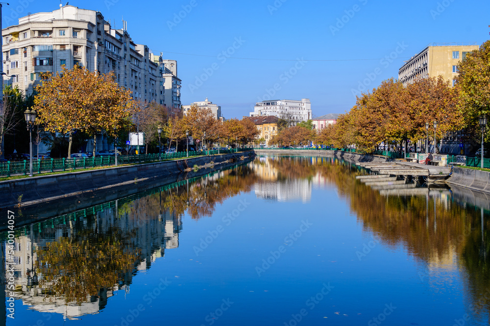 Landscape with Dambovita river, old buildings and yellow, orange and brown leaves in large trees in the center of Bucharest, Romania, in a sunny autumn day.