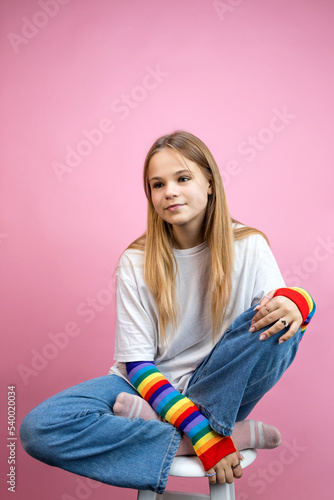 A pensive young girl sits on a white chair. pink background