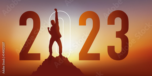 Carte de voeux 2023 montrant un homme levant le poing en signe de la victoire après avoir atteint son objectif en arrivant au sommet d’une montagne. photo