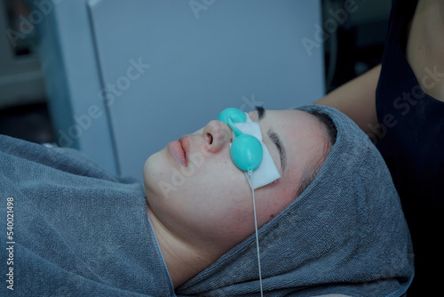 Young woman doing bio light red light therapy on her face Woman blindfolded and irradiated facial skin care  Bio light therapy in beauty clinic   light for facial rejuvenation  Beauty concepts.