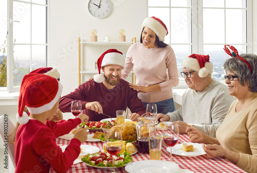 Young woman takes care of her family during traditional Christmas holiday breakfast meal at home. Happy multi-generational family with seniors and younger family members sitting together at table.