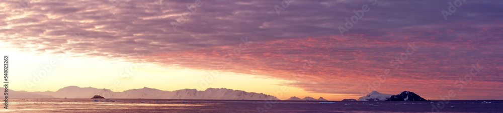 Panorama of a colorful sunset over mountains and a field of floating icebergs at Cierva Cove, Antarctica