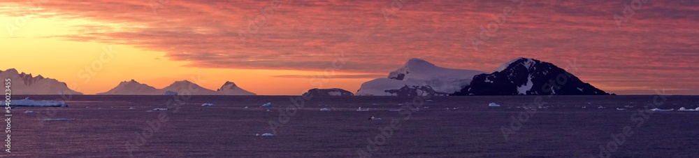 Panorama of a colorful sunset over mountains and a field of floating icebergs at Cierva Cove, Antarctica