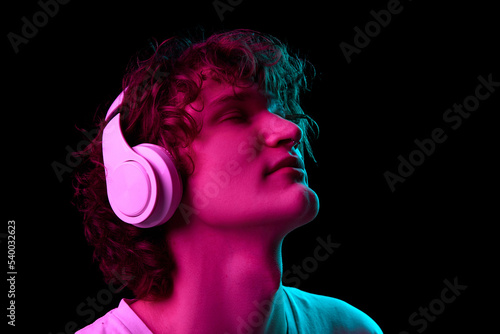 Calm, dreams and relax. Closeup portrait of student in white tee listening to music isolated on dark background in neon. Concept of music, facial expression, youth