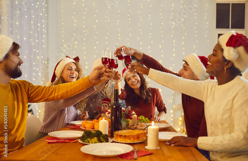 Quadro em tela Smiling multiethnic friends sit at table clink glasses cheers celebrate inter holidays with Christmas dinner