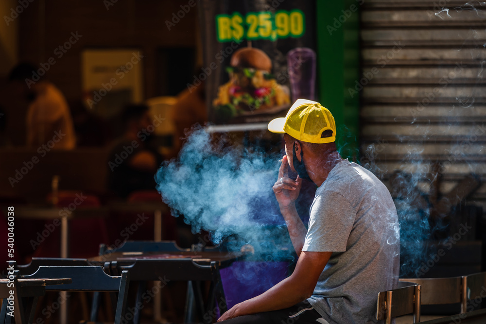 Young black Brazilian man smoking a cigarette outside of a burger restaurant at Savassi, Belo Horizonte, Brazil.