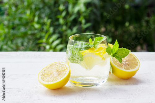 Homemade lemonade with lemon, mint and ice cubes in a glass on the white wood table with lemons. © Philippova
