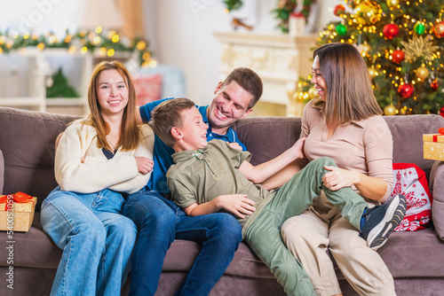 Merry Christmas. A happy loving family is sitting on the couch and having fun during the New Year holidays. Parents and children hug each other, are in the living room decorated for the holiday.