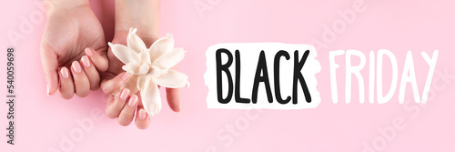Black Friday sign on pink background banner with female hands with beautiful manicure - pink nude nails with white dried flower, wide panoramic header. Shopping concept