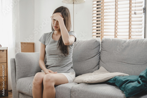 Headache. asian woman touching forehead having headache migraine upset with problem feel stressed sitting on couch in living room at home, people painful, depression, medical and health care concept