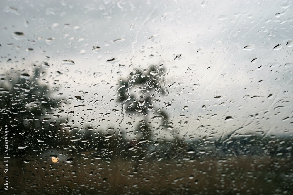 Glasscheibe mit Regentropfenmuster vor braunem Ackerfeld, goldgelb funkelndem Autolicht, zwei Bäumen vor Himmel bei Regen und Sturm am Mittag im Herbst Glasscheibe mit Regentropfenmuster vor braunem Ackerfeld, goldgelb funkelndem Autolicht, zwei Bäumen vor Himmel bei Regen und Sturm am Mittag im Herbst