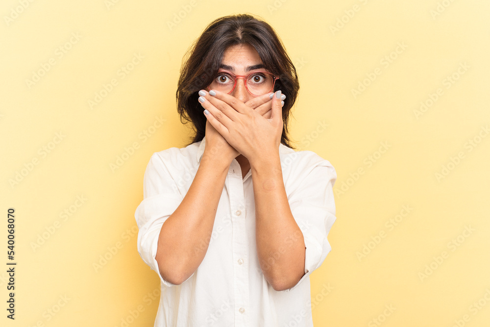 Young Indian woman isolated on yellow background shocked covering mouth with hands. Young Indian woman isolated on yellow background shocked covering mouth with hands.