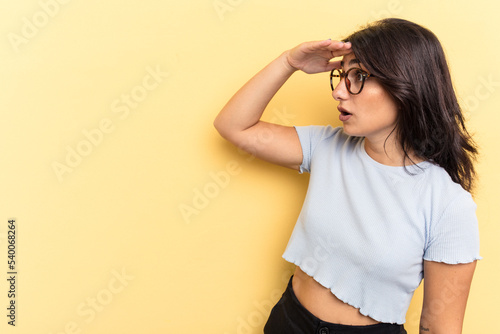 Fotografie Young Indian woman isolated on yellow background looking far away keeping hand on forehead