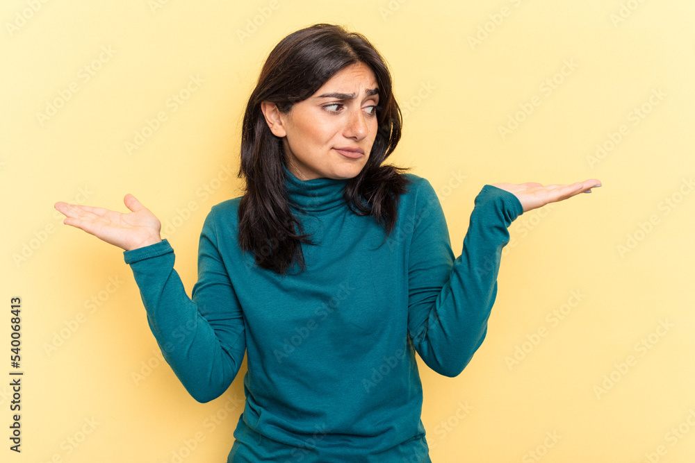 Young Indian woman isolated on yellow background confused and doubtful shrugging shoulders to hold a copy space. Young Indian woman isolated on yellow background confused and doubtful shrugging shoulders to hold a copy space.