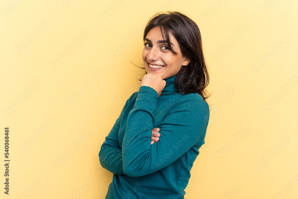 Young Indian woman isolated on yellow background smiling happy and confident, touching chin with hand.
