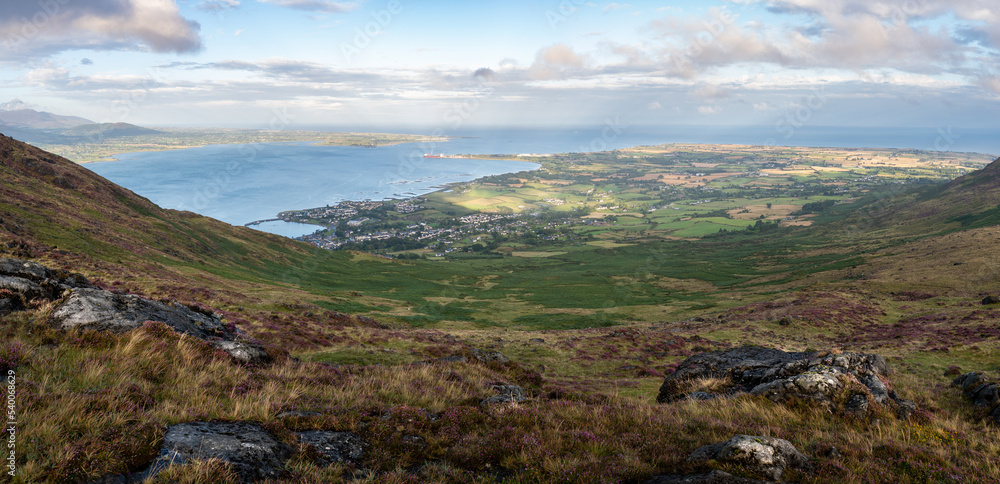 Panoramic view from the top on fields in many shades of green in a valley in the Irish rural countryside. Bay and sea in the background