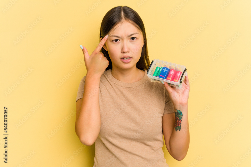 Young Asian woman holding batteries to recycle them isolated on yellow background showing a disappointment gesture with forefinger. Young Asian woman holding batteries to recycle them isolated on yellow background showing a disappointment gesture with forefinger.