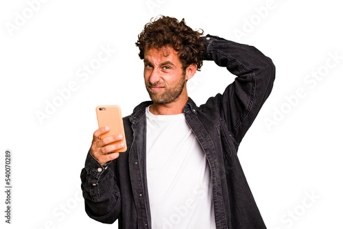 Fotografía Young caucasian man using mobile phone isolated touching back of head, thinking and making a choice