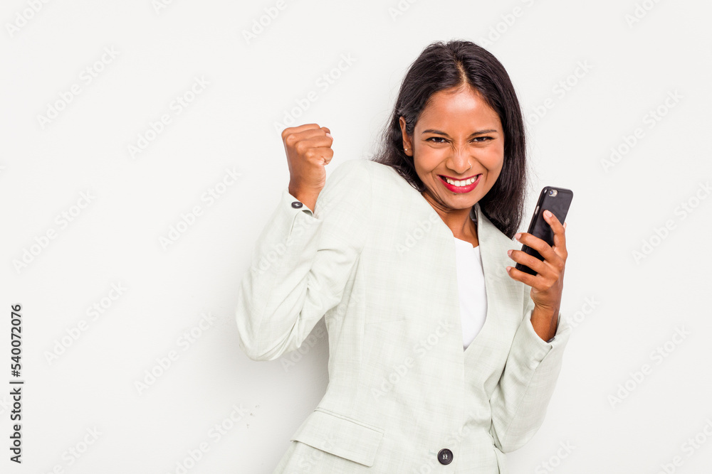 Young business Indian woman holding a mobile phone isolated on white background raising fist after a victory, winner concept. Young business Indian woman holding a mobile phone isolated on white background raising fist after a victory, winner concept.