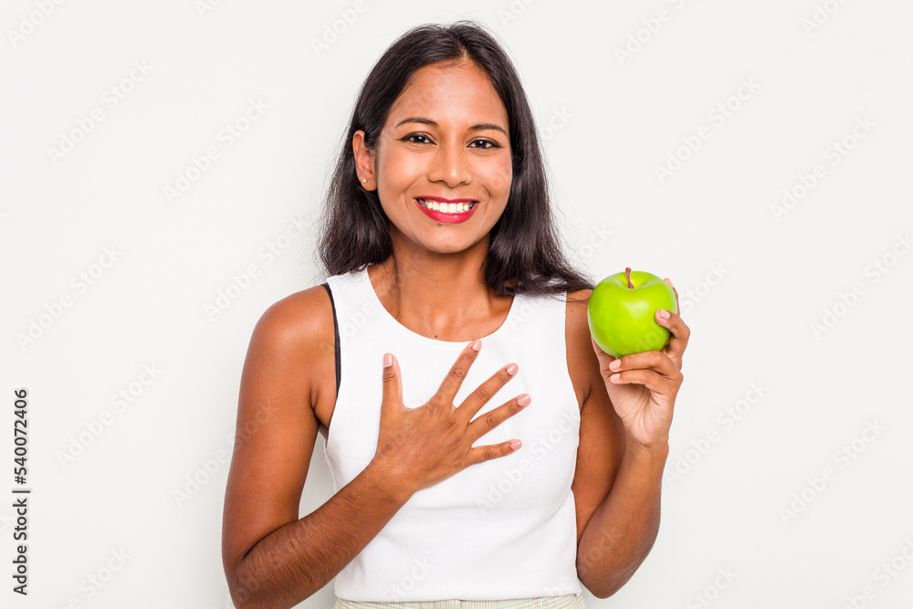 Young Indian woman holding an apple isolated on white background laughs out loudly keeping hand on chest. Young Indian woman holding an apple isolated on white background laughs out loudly keeping hand on chest.
