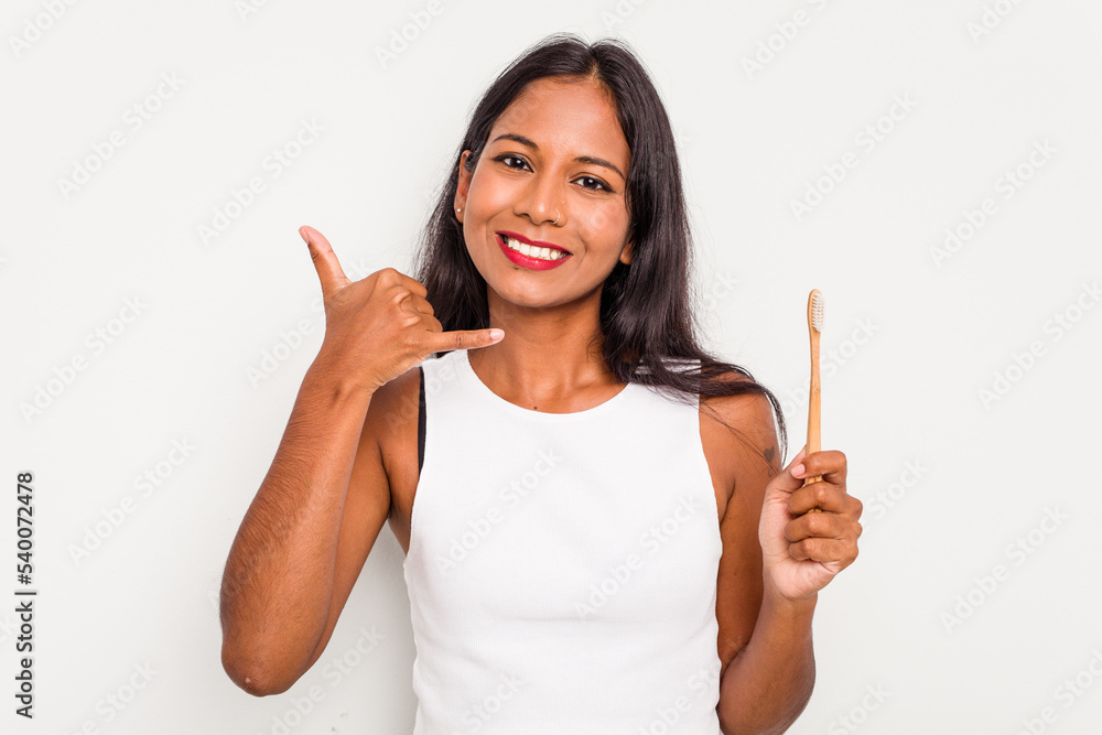 Young Indian woman brushing teeth isolated on white background showing a mobile phone call gesture with fingers. Young Indian woman brushing teeth isolated on white background showing a mobile phone call gesture with fingers.