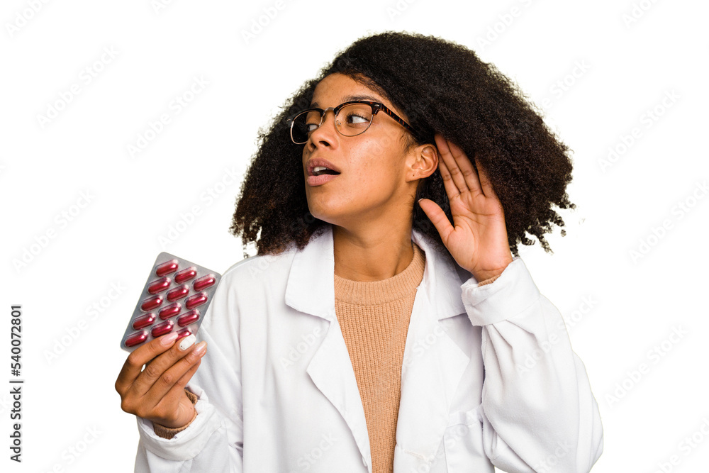 Young pharmacist African American woman holding a tablet of pills isolated trying to listening a gossip. Young pharmacist African American woman holding a tablet of pills isolated trying to listening a gossip.