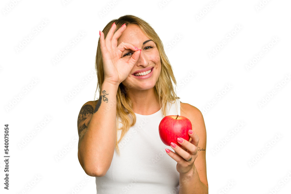 Young caucasian woman holding an apple isolated on green chroma background excited keeping ok gesture on eye. Young caucasian woman holding an apple isolated on green chroma background excited keeping ok gesture on eye.