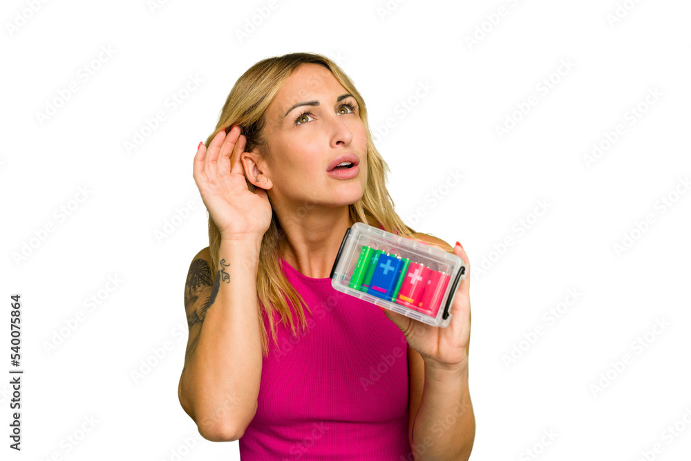 Young caucasian woman holding battery box isolated on green chroma background trying to listening a gossip. Young caucasian woman holding battery box isolated on green chroma background trying to listening a gossip.