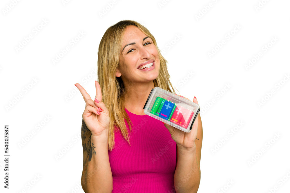 Young caucasian woman holding battery box isolated on green chroma background joyful and carefree showing a peace symbol with fingers. Young caucasian woman holding battery box isolated on green chroma background joyful and carefree showing a peace symbol with fingers.
