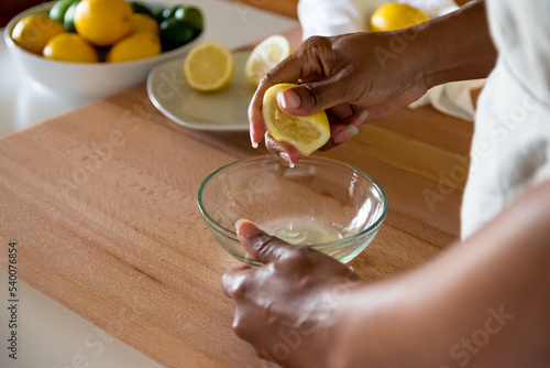 African American woman, Black woman hand squeezing fresh lemon juice into glass bowl photo