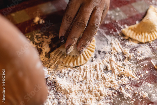 Imagen horizontal de cerca de las  manos de una mujer irreconocible preparando algunas empanadas. 
