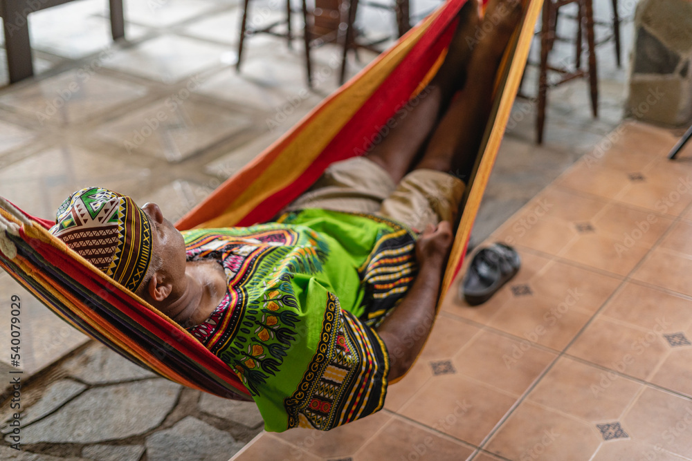 Imagen horizontal de un hombre latino adulto acostado en una hamaca de tela en su casa descansando. 