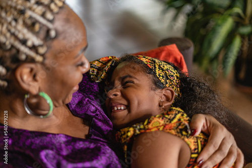 Imagen horizontal de una madre y su hija afrocaribeñas muy alegres y sonrientes jugando juntas en el interior de su casa. 