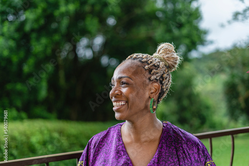Retrato horizontal de una hermosa mujer afrocaribeña muy sonriente en el exterior de su casa  con un vestido caribeño muy colorido disfrutando de un día de verano. photo