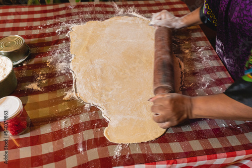 Imagen horizontal de una mujer afrocaribeña irreconocible aplanando con un rodillo de madera un trozo de masa para preparar algunos bocadillos caribeños para su negocio.  photo