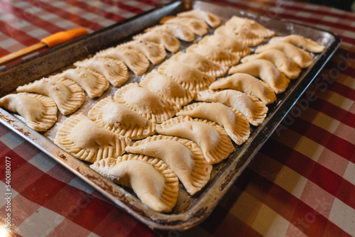 Imagen horizontal de unas deliciosas empanadas crudas al estilo caribeño en una bandeja sobre una mesa en el interior de una casa listas para ser horneadas. photo