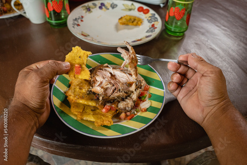 Imagen horizontal de cerca de un plato  con una deliciosa comida caribeña sobre una mesa mientras un hombre irreconocible come.
