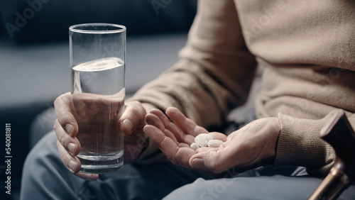 cropped view of senior man with dementia holding pills and glass of water.