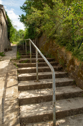 escalier ext  rieur en b  ton  avec une rampe m  tallique et une pente douce pour les cycles et les trotinettes ou les poussettes d enfants  Verdure  arbres et buissons sauvages