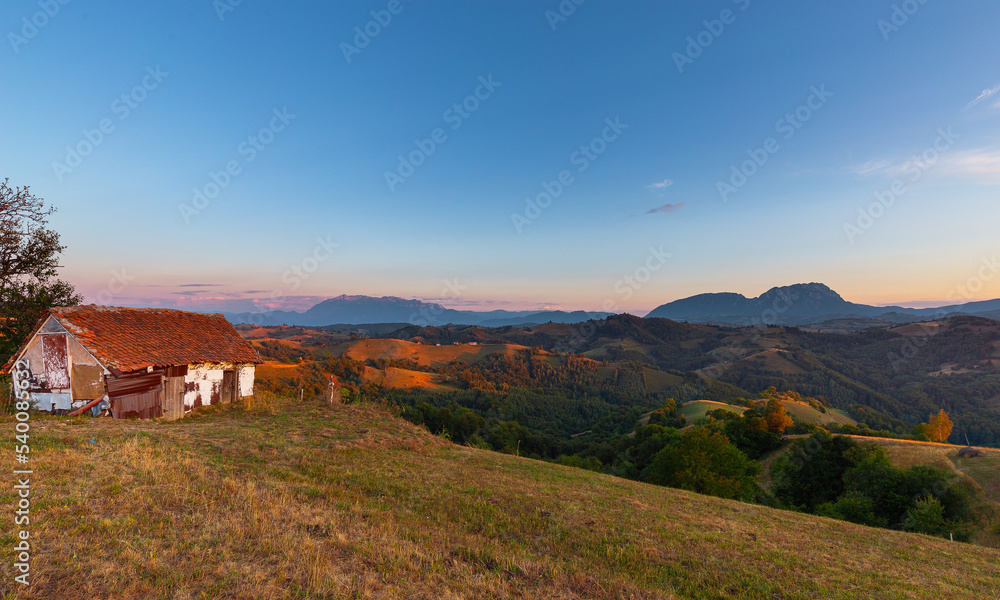 Barn on top of hill overlooking deep valley and mountain range on the horizon