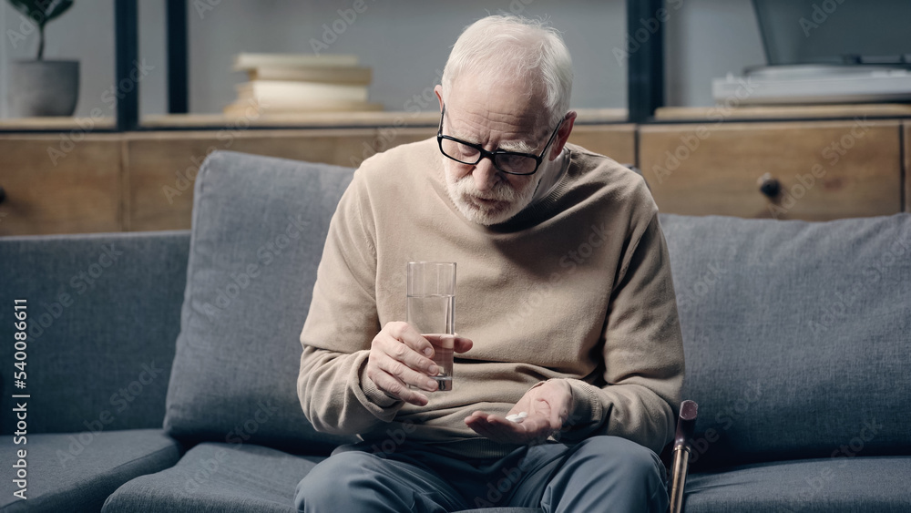 Senior man with dementia holding pills and glass of water at home.