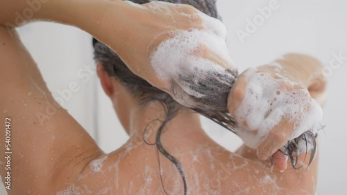 Naked woman washes her hair with shampoo and looks at palm with hair that has fallen out. Losing hair because of stress, bad ecology, unhealthy lifestyle. Morning routine in modern urban apartment.