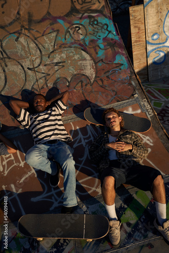 Two young non-binary skateboarders in skatepark hanging out
